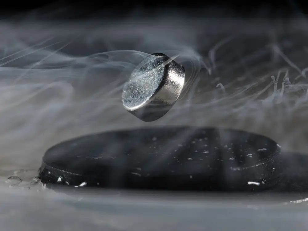 A magnet hovering above a superconductor. Persistent electric current flows on the surface of the superconductor, forming an electromagnet that repels the magnet.  (Image from Insider)